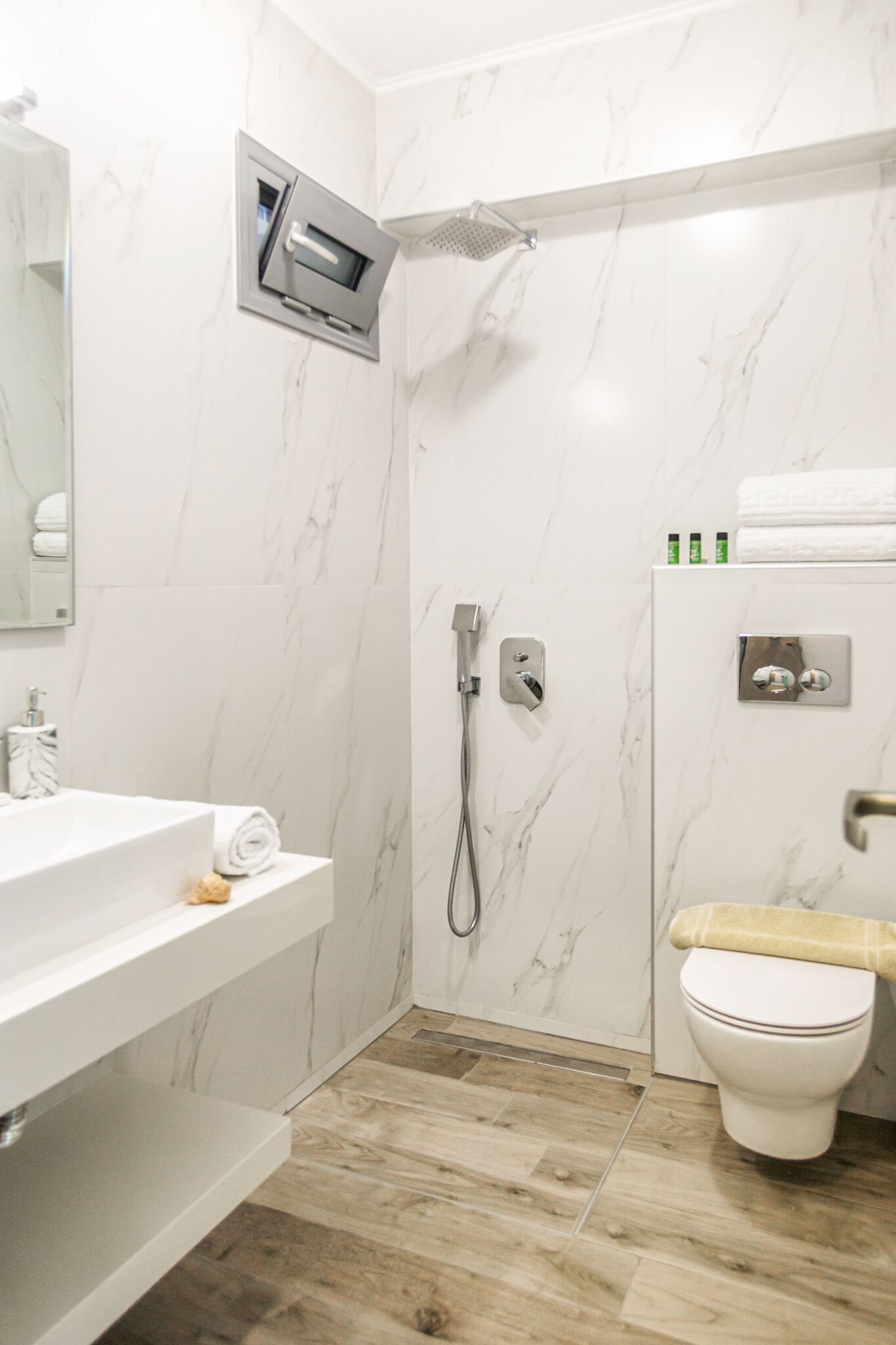 A modern bathroom with a marble wall, a shower, a toilet, and a sink with a towel.