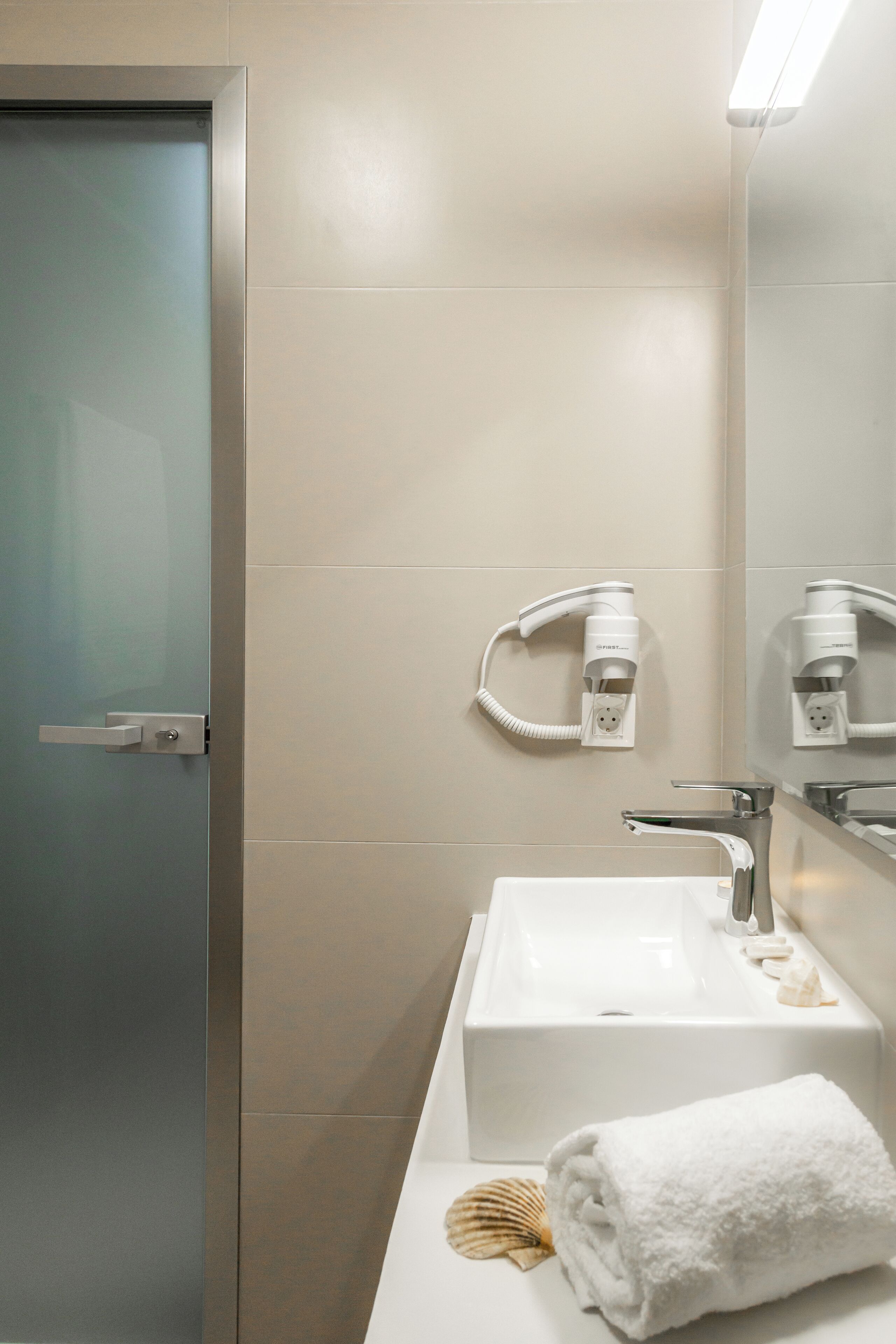 A modern bathroom with a white sink, a towel, and a hairdryer mounted on the wall.