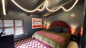 Un dormitorio con cama, un escritorio, una silla, una ventana con persianas, un cuadro en la pared y una lámpara en el techo.