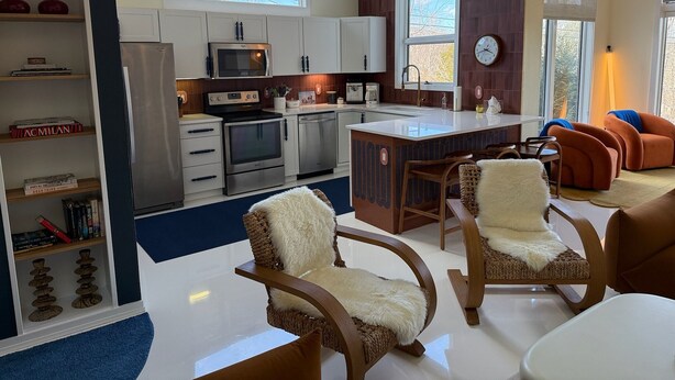 Una cocina moderna con armarios blancos, microondas, horno y lavavajillas. Hay un comedor con sillas de madera y una mesa blanca.
