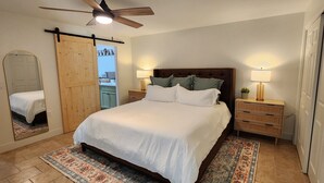 Une chambre à coucher comprenant un lit, des tables de chevet, un ventilateur de plafond et un grand miroir.