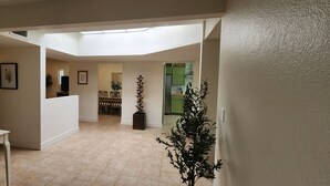Un vaste hall d’entrée doté d’un haut plafond et d’une verrière, qui mène à une salle à manger avec une table et des chaises en bois.