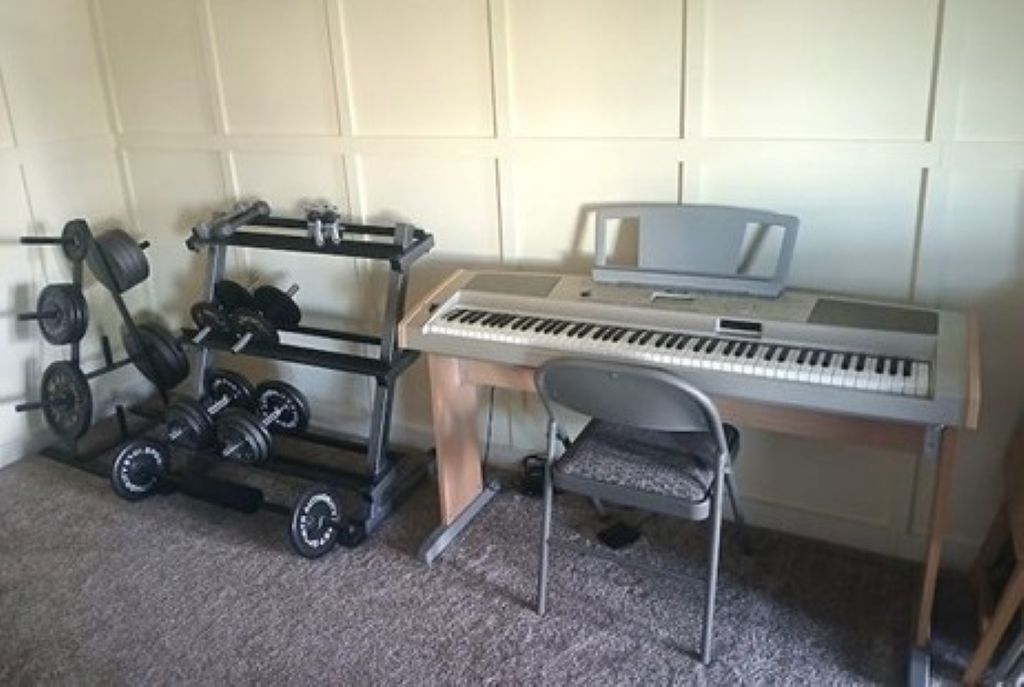Une pièce comprenant un piano, une chaise et un porte-haltères avec des poids.