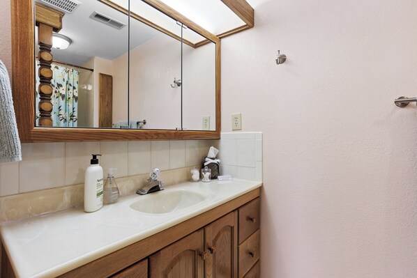 Un baño con tocador de madera, lavabo blanco y espejo encima.