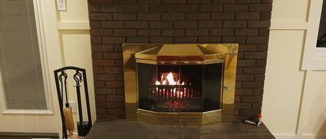 A fireplace with a brick surround and a glass front, featuring a visible fire.
