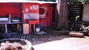 A red building with a brick floor, a sink, and a toilet. There is a fire pit and a tree nearby. - hostel mi lugar (Mar del Plata)