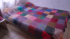 A bed with a colorful quilt and a wooden headboard. - hostel mi lugar (Mar del Plata)