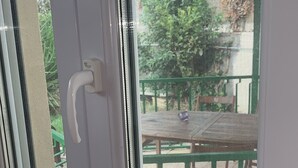Una ventana con marco y manija blancos, que da a un espacio exterior con una mesa y sillas verdes.