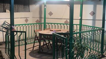 Een buitenruimte met een tafel en stoelen, omgeven door groene hekken en een bakstenen muur.