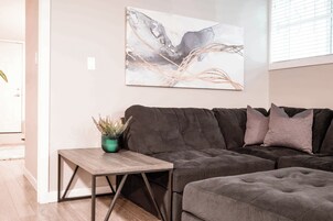 A modern living room with a dark brown sectional sofa, a small wooden side table with a green plant, and a large abstract painting on the wall.