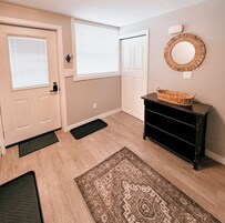 A hallway with a wooden floor, a black dresser with a woven basket, a patterned rug, and a round mirror on the wall.