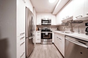 A modern kitchen with stainless steel appliances, white cabinetry, and a tiled backsplash.