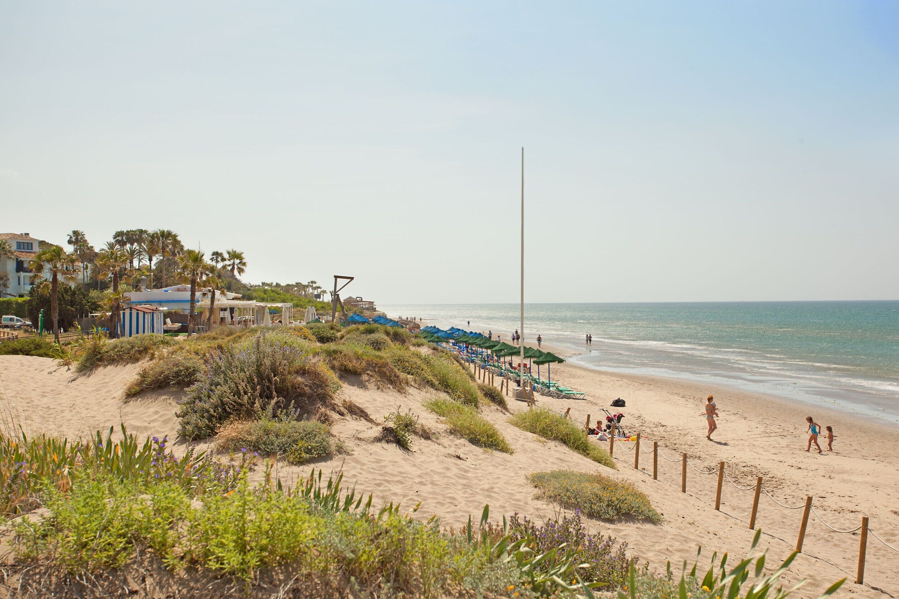 A beach with sand dunes, beach umbrellas, and a few people.
