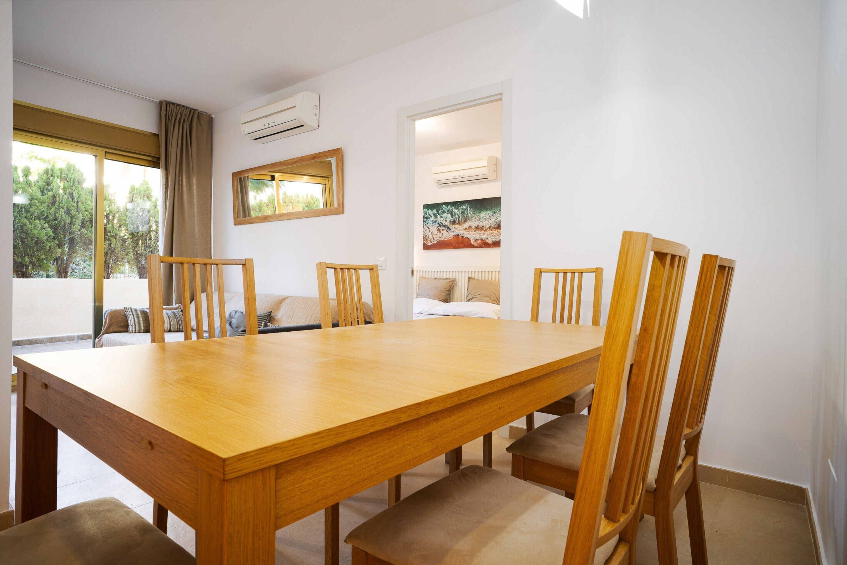 A dining area with a wooden table and chairs, a large window with curtains, and artwork on the walls.