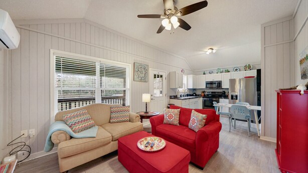 A living room with a beige sofa and a red sofa, a ceiling fan, and a kitchen in the background. - Oak St Oasis - Minutes from Downtown and the beach! (Downtown St. Augustine)