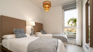 A hotel room with two beds, a large window with a view of a pool and palm trees, a wall-mounted lamp, and a textured ceiling light fixture. - Nice Apartment With Shared Pool (Estepona)
