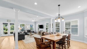 Amplia sala de estar con una mesa de comedor de madera, asientos cómodos y ventanas grandes con persianas.