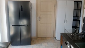Kompakti keittiö, jossa on musta jääkaappi, puinen ovi ja valkoiset kaapit.