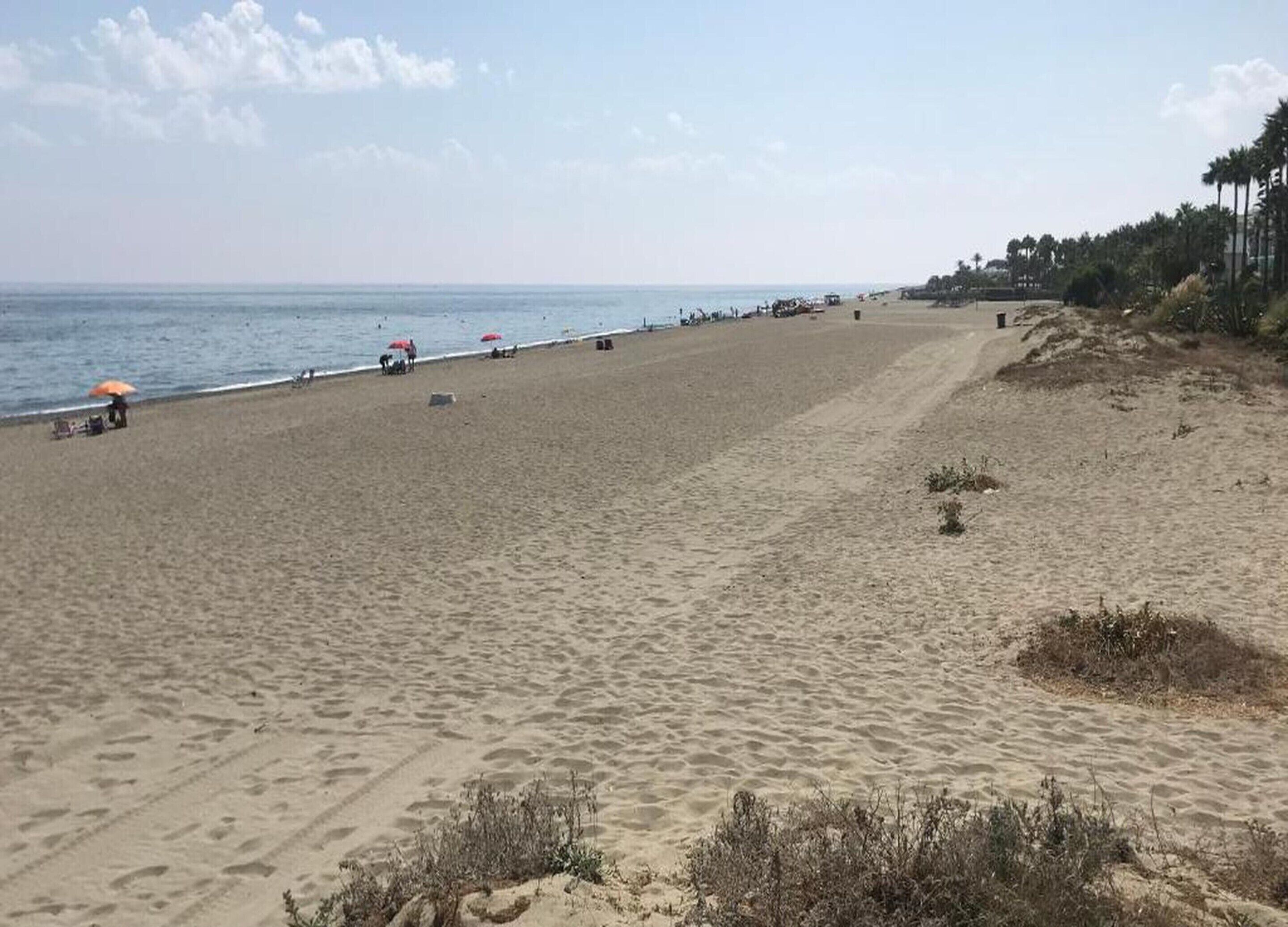 A wide sandy beach with a few umbrellas and people.
