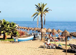 Une plage bordée de palmiers, un bateau et des parasols en chaume.