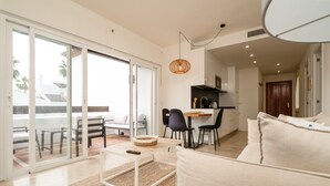 A modern living room with a sofa, a coffee table, and a dining area with chairs. - Cozy Garden Apartment by Sea (Estepona)