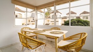 Un espace repas comprenant une table et des chaises, de grandes fenêtres et une vue sur les bâtiments.