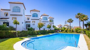 Une piscine entourée d’une pelouse bien entretenue, avec un bâtiment blanc doté de nombreuses fenêtres et de balcons en arrière-plan.