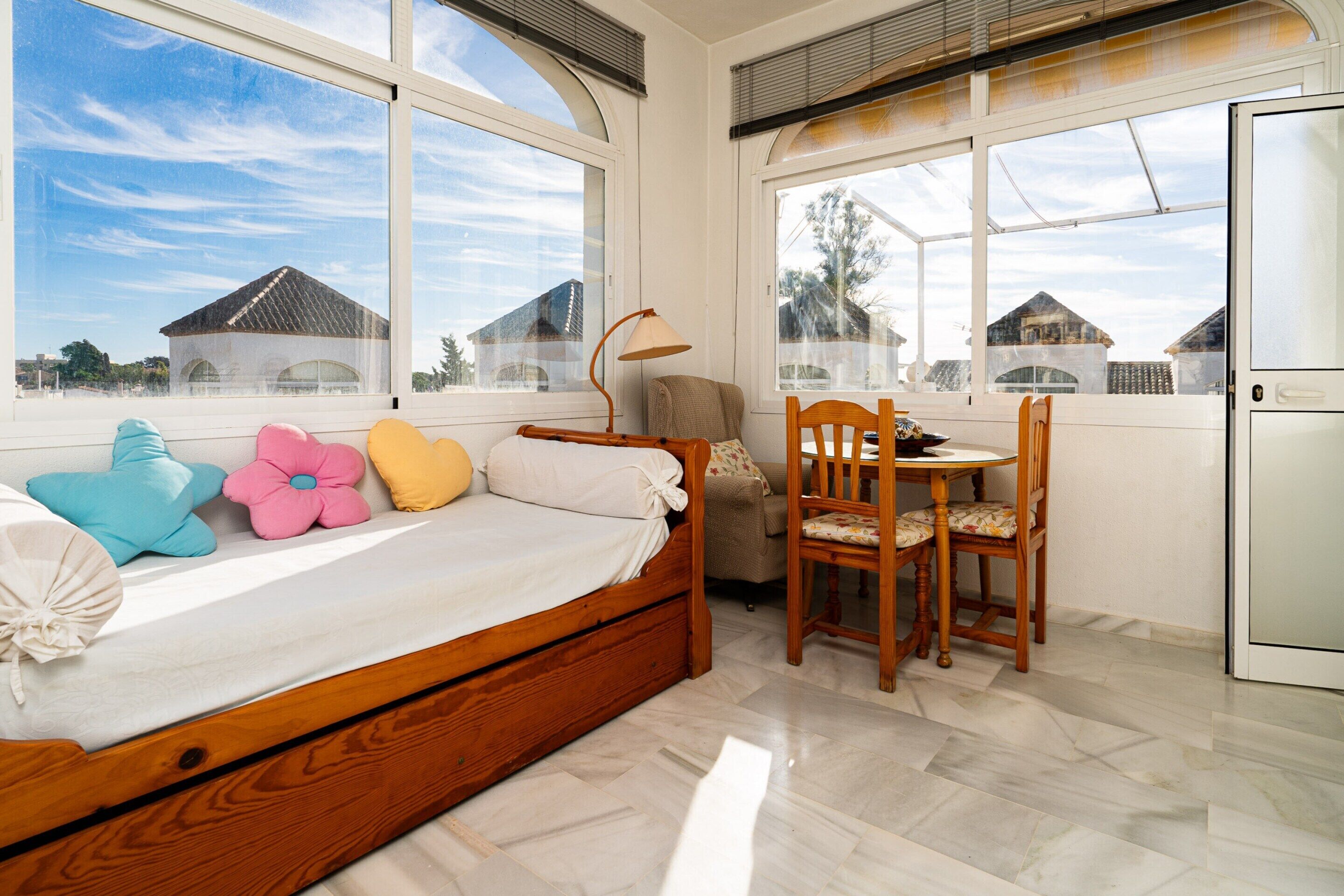Ein Schlafzimmer mit Bett, Stuhl, Tisch und großen Fenstern.