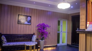 Een receptiegedeelte met een houten wand, een bank, een tafel, een plant in pot en een deur.