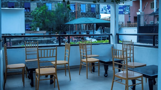 Een terras buiten met bamboe stoelen en tafels, met uitzicht op een stadsgezicht met gebouwen en groen.