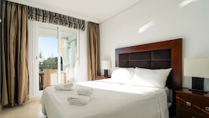 Een hotelkamer met een groot bed, een houten hoofdbord, een nachtkastje met lamp en uitzicht door een schuifdeur.