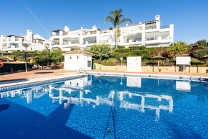 Une piscine à l’eau d’un bleu cristallin, entourée d’un bâtiment blanc doté de balcons et d’un petit jardin.