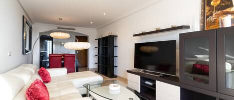 Een moderne woonkamer met een bank, een glazen salontafel, een flatscreen televisie en een zwarte entertainmentkast.