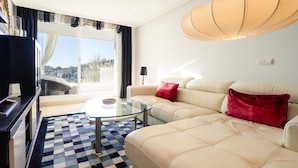 Een moderne woonkamer met een glazen salontafel, een bank met rode kussens, een televisie en een groot raam met gordijnen.