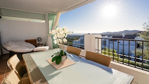 Een balkon met een tafel, stoelen, een potplant en een bed.