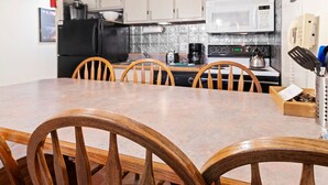Une cuisine avec des chaises en bois, une table à manger, un réfrigérateur noir, un four à micro-ondes blanc et une cuisinière.