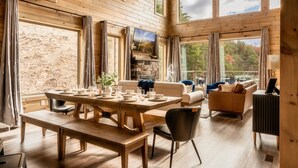 Un vaste espace de vie doté d  ’un plancher en bois, d’une cheminée en pierre et de grandes fenêtres offrant une vue sur l’extérieur.
