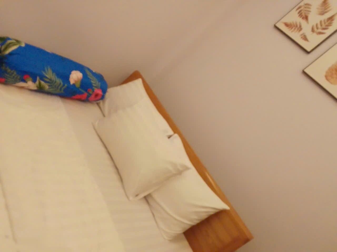 A bed with a blue floral bedspread, a white pillow, and a wooden headboard.