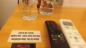 Ein Tisch mit Fernbedienung, einem Schild für '102 House', einem Netflix-Logo und zwei Wasserflaschen mit Minzblättern.