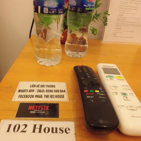 A table with a remote control, a sign for '102 House', a Netflix sign, and two water bottles with mint leaves. - 102 house (Ho Chi Minh City)
