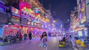 Eine beleuchtete Straße bei Nacht mit verschiedenen Geschäften und Schildern, darunter ein auffälliges Schild mit 'Miss Saigon'.