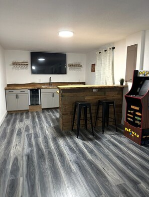 A modern kitchen with a wooden island, bar stools, a flat-screen TV, and a Pac-Man arcade machine.