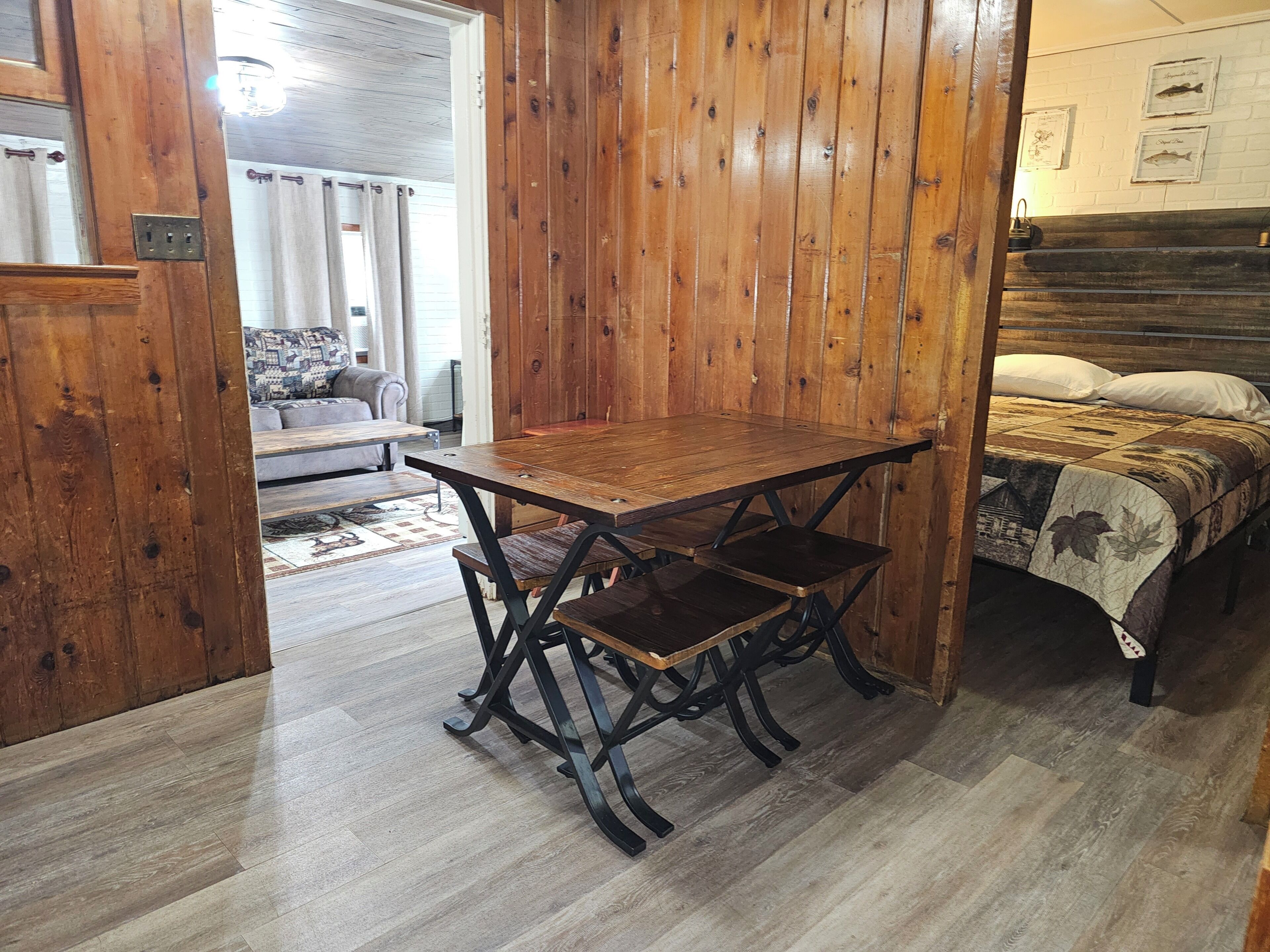 A wooden dining table with benches in a room with wooden walls and a bed with a patterned bedspread.