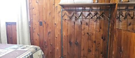 Una habitación de madera con una cama, un escurridor de metal con toallas y una pared de madera.