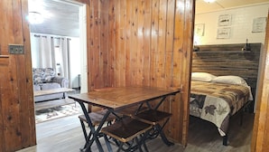 Una habitación con paneles de madera, una mesa y sillas de madera, una cama con colcha estampada y una pared de ladrillo blanco con ilustraciones de peces.