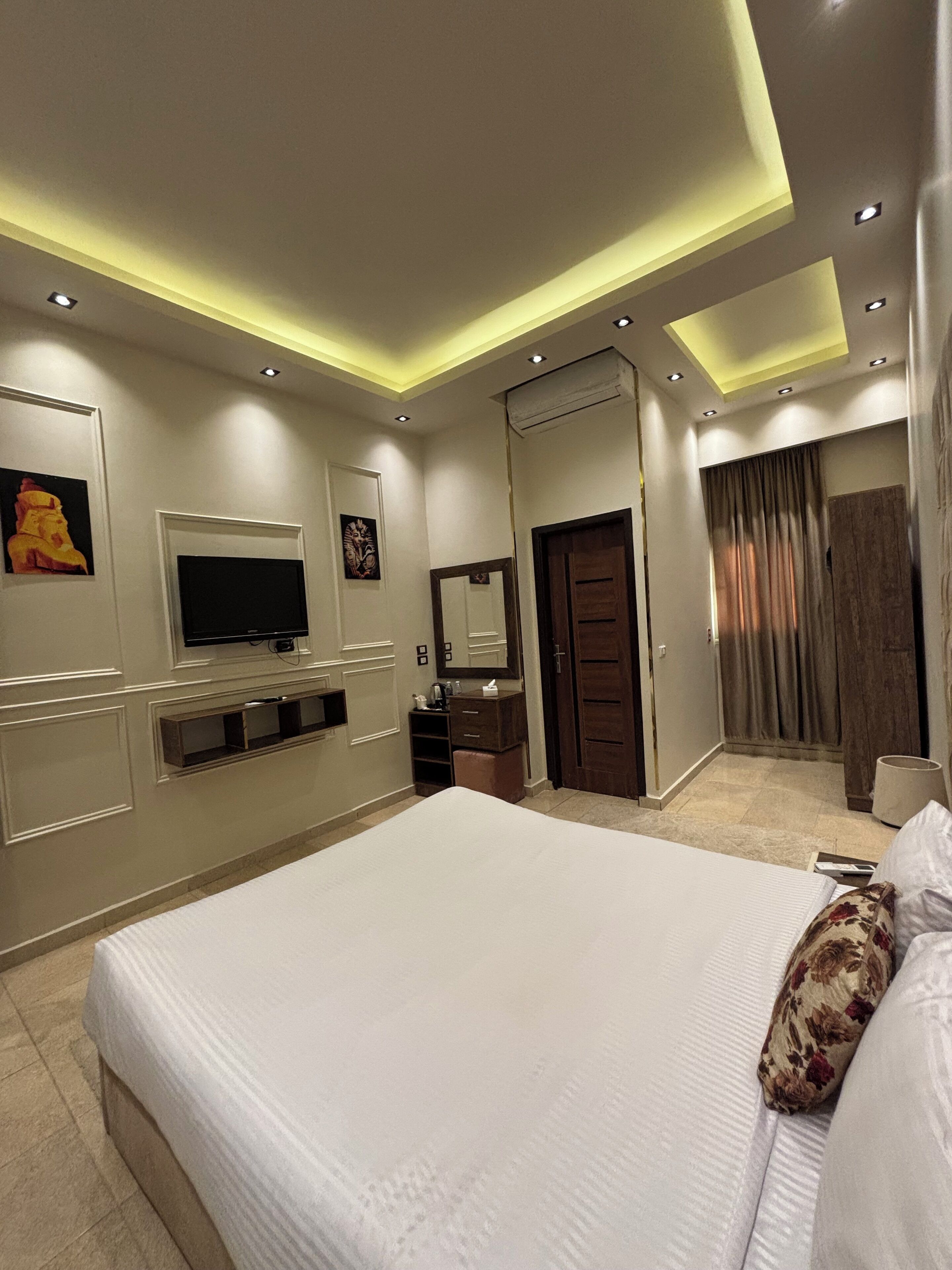 A modern hotel room with a large bed, a flat-screen TV, a vanity with a mirror, and a wardrobe.