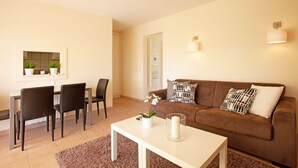A living room with a brown sofa, two black chairs, a white coffee table, and a small white table with a plant and candle. - Holiday Home Marbella Near Sand Beach (Marbella)
