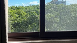 A window with a view of a building with a thatched roof structure amidst dense greenery. - Modern&Quiet full Apartment with Pool in Punta Sur, relax and enjoy this place (Isla Mujeres)