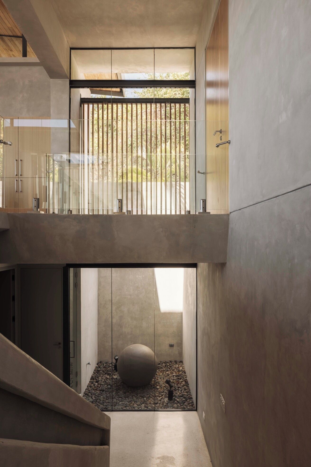 Un interior modern amb una escala de formigó, una barana de vidre i una gran esfera al terra.