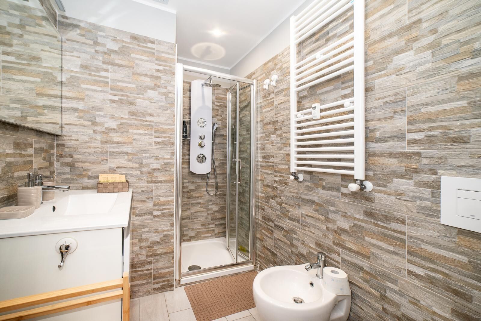 Un baño moderno con ducha de mampara de vidrio, lavamanos blanco y toallero.
